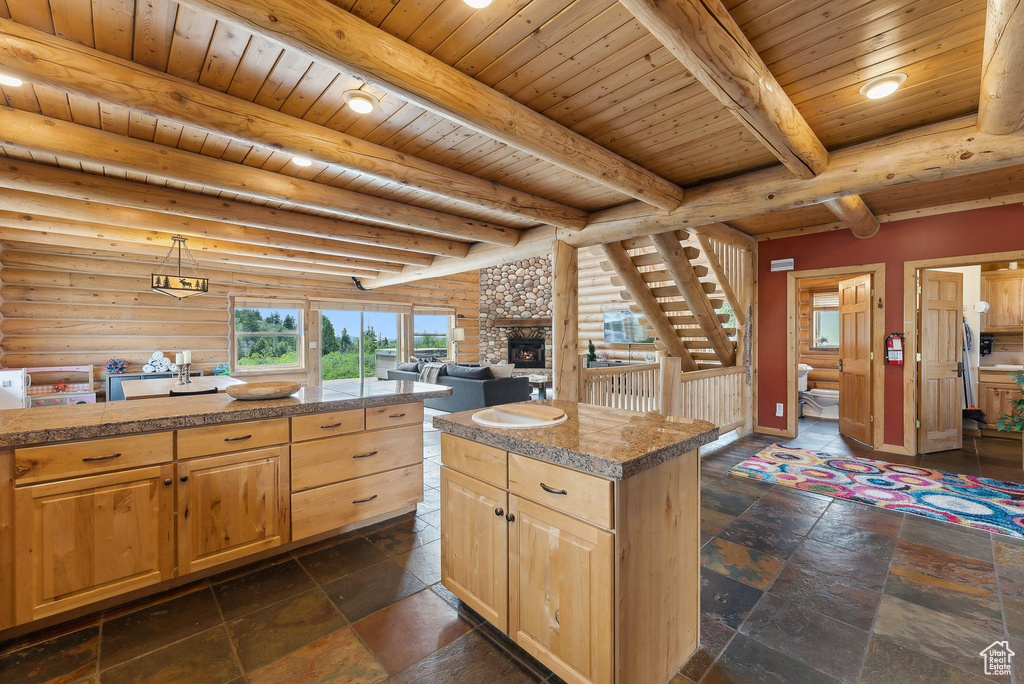 Kitchen featuring tile countertops, light brown cabinetry, wooden ceiling with exposed beams, log walls, and a stone fireplace