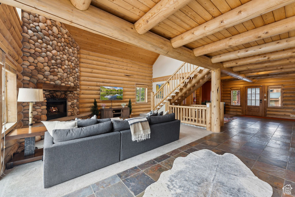 Living area featuring a fireplace, wood ceiling, stairway, log walls, and stone tile flooring