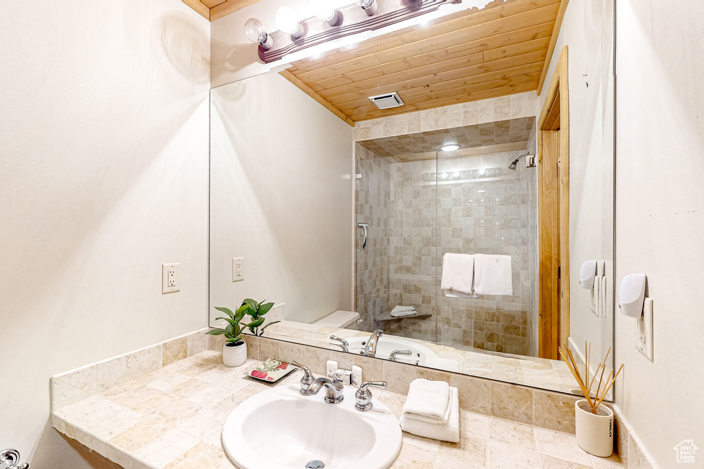 Bathroom featuring a sink, tiled shower, wooden ceiling, and toilet