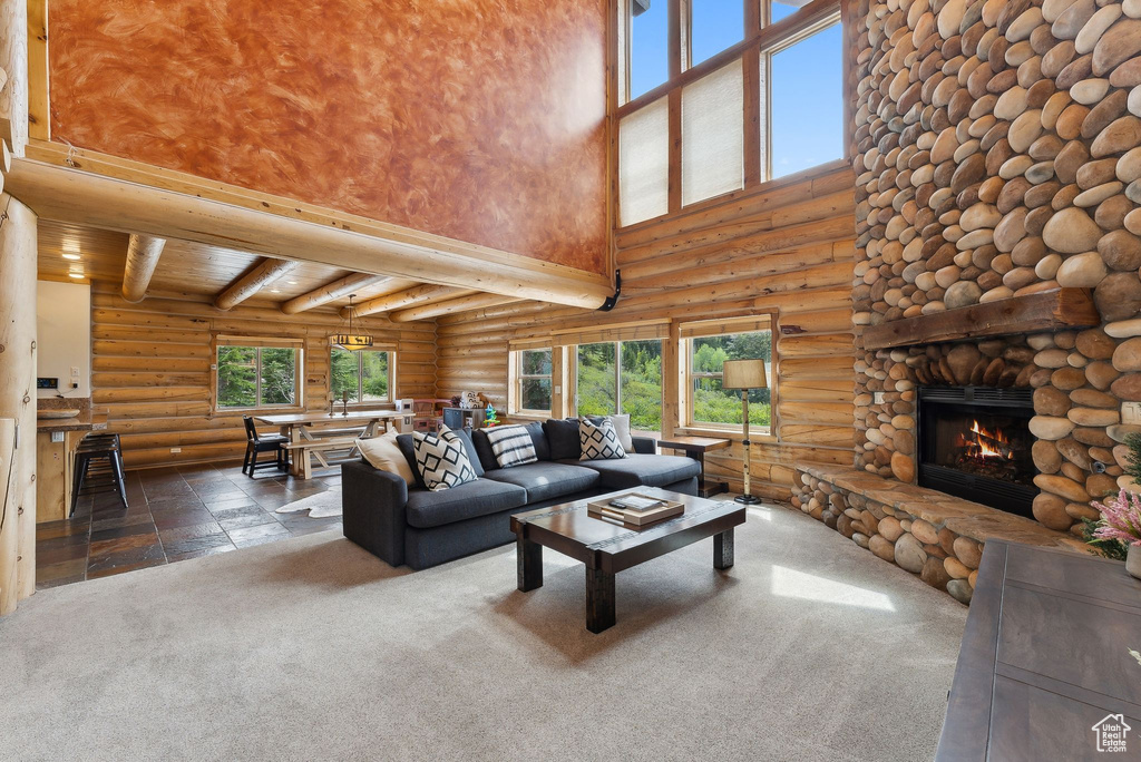 Carpeted living area featuring a towering ceiling, log walls, a fireplace, beamed ceiling, and stone finish floors