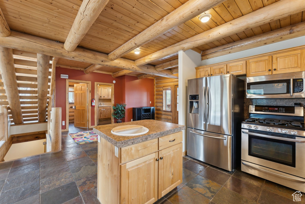 Kitchen with appliances with stainless steel finishes, a center island, light brown cabinetry, wood ceiling with exposed beams, and stone tile flooring