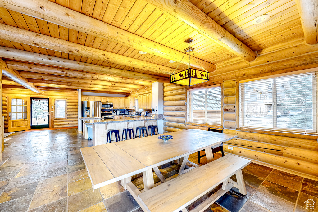 Dining space with wood ceiling with exposed beams, healthy amount of natural light, log walls, and stone tile floors