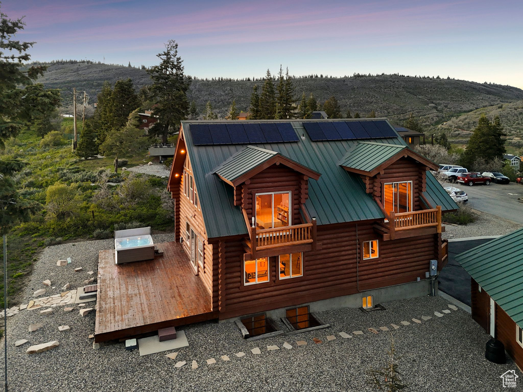 Back of house with log exterior, a deck with mountain view, metal roof, and roof mounted solar panels