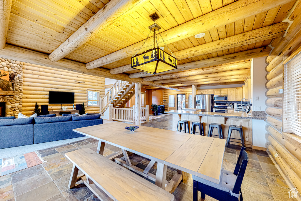 Dining space featuring wood ceiling with exposed beams, rustic walls, and stone tile flooring