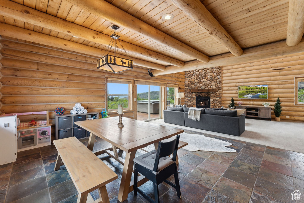 Dining space featuring wood ceiling with exposed beams, a stone fireplace, stone tile floors, and log walls