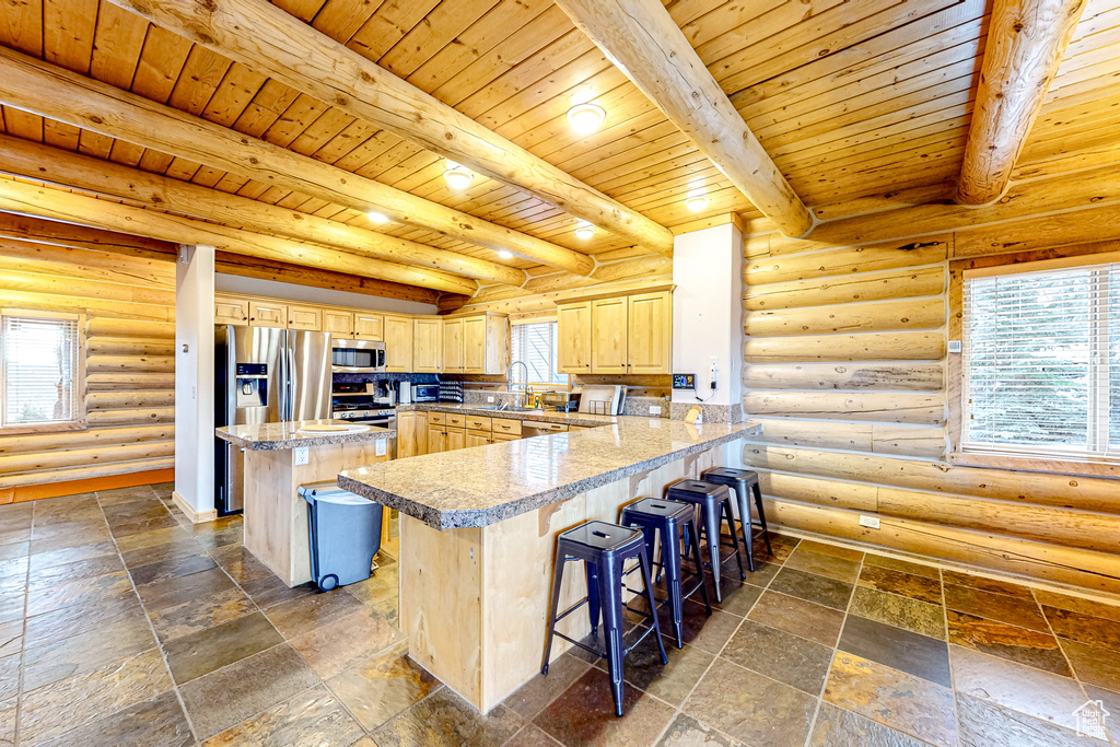 Kitchen featuring light brown cabinetry, a sink, stainless steel appliances, a breakfast bar, and wood ceiling with exposed beams