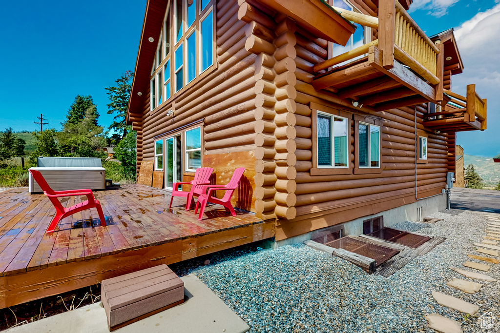 View of side of property with log exterior, a covered hot tub, a balcony, and a deck
