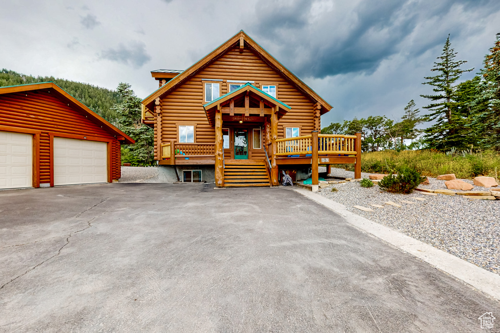 Log-style house with log siding, a wooden deck, an outbuilding, and a detached garage