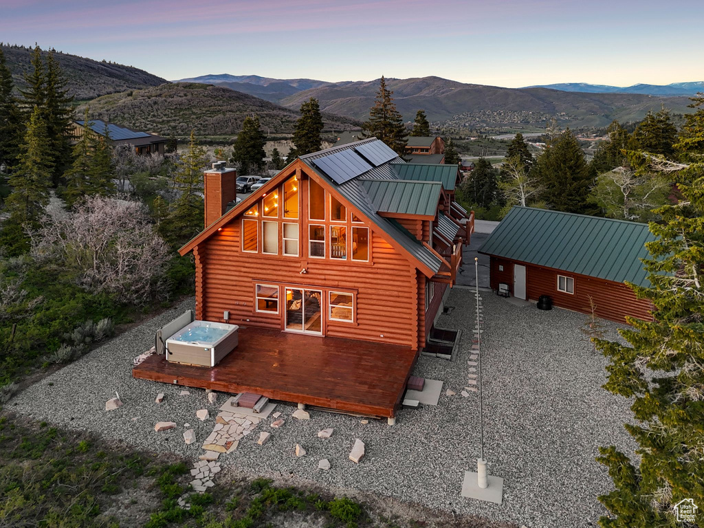 Back of house at dusk featuring a chimney, log exterior, a deck with mountain view, and metal roof