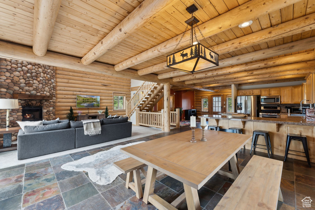 Dining area with wooden ceiling with exposed beams, a stone fireplace, log walls, stairway, and stone tile floors