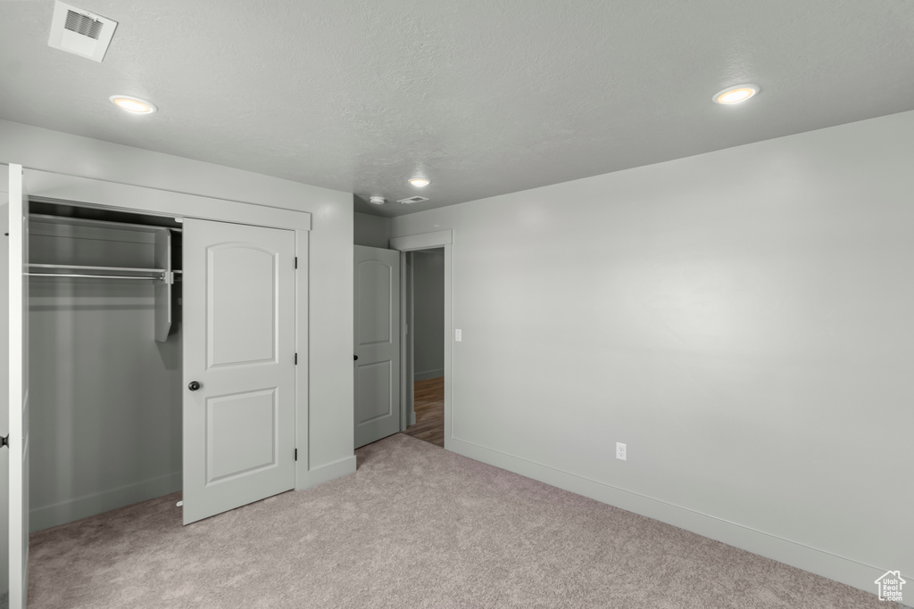 Unfurnished bedroom featuring light carpet, a closet, baseboards, recessed lighting, and a textured ceiling