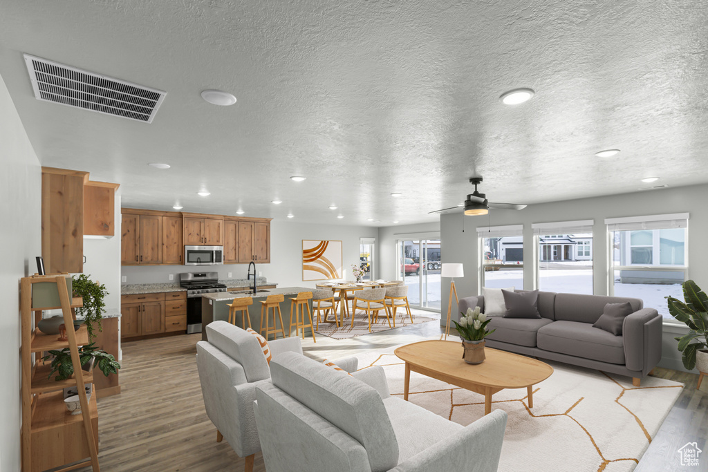 Living room featuring light wood finished floors, recessed lighting, ceiling fan, and a textured ceiling