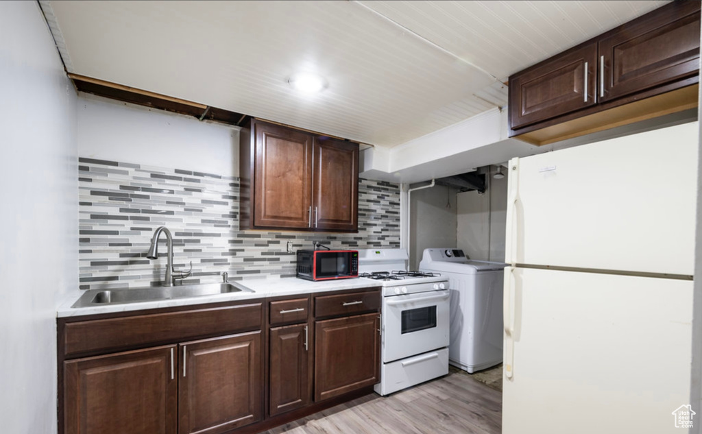 Kitchen with a sink, white appliances, washer / clothes dryer, light countertops, and backsplash