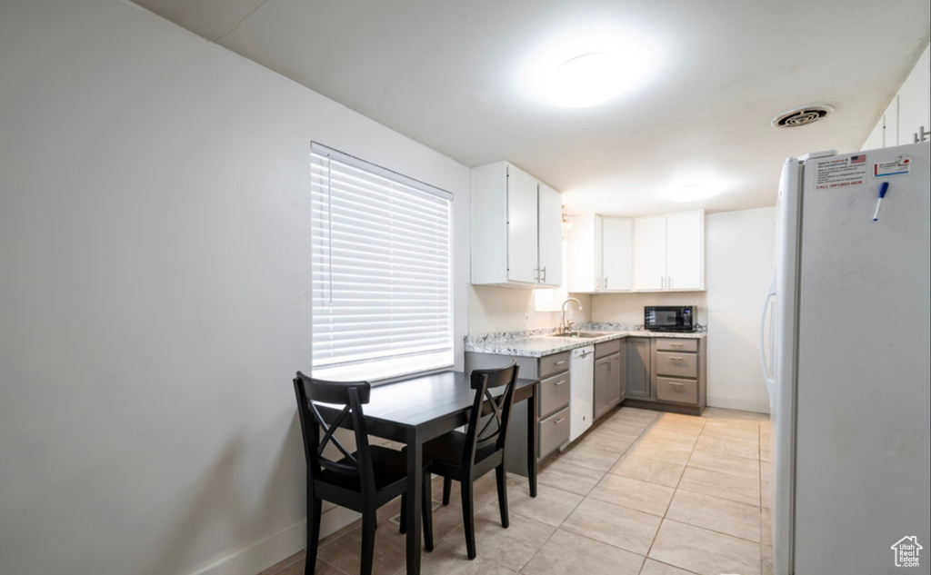 Kitchen with white appliances, white cabinetry, a sink, light tile patterned flooring, and light stone countertops