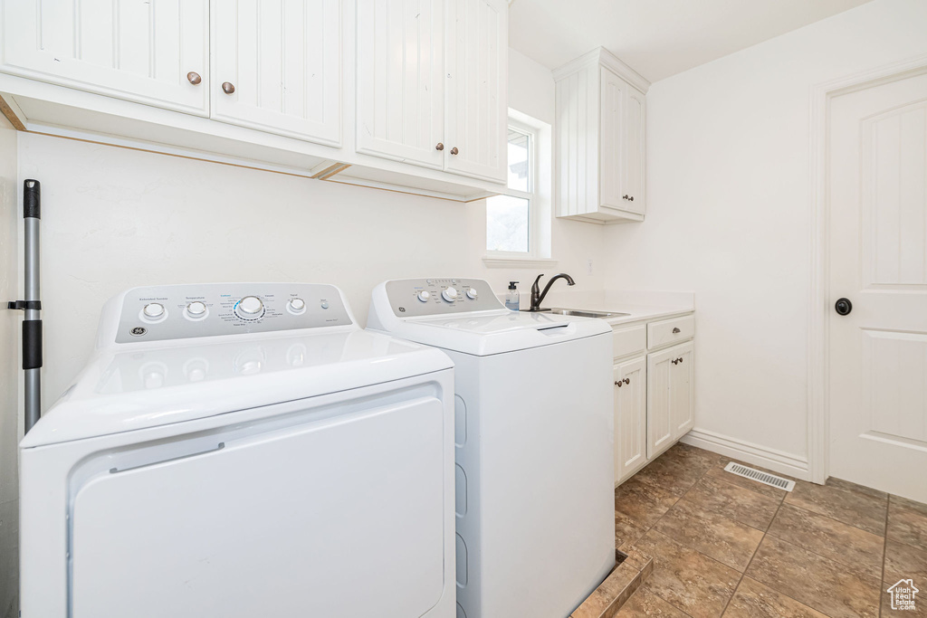 Washroom featuring washer and clothes dryer, cabinet space, stone finish floors, and baseboards