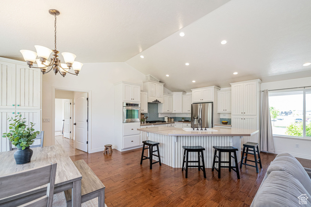 Kitchen featuring stainless steel appliances, white cabinets, lofted ceiling, a spacious island, and a kitchen breakfast bar