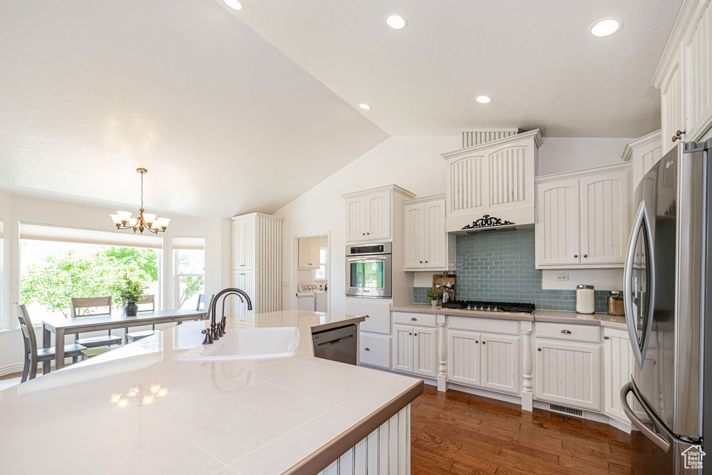 Kitchen featuring appliances with stainless steel finishes, a sink, separate washer and dryer, lofted ceiling, and a chandelier