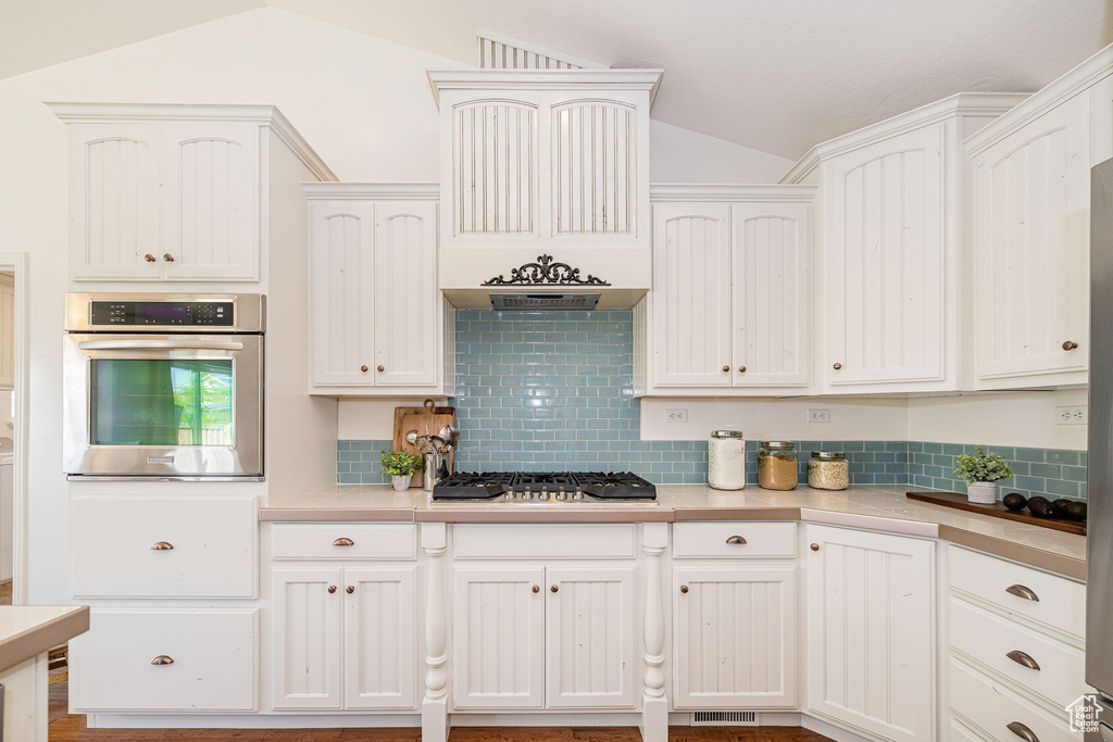 Kitchen featuring stainless steel appliances, lofted ceiling, light countertops, tasteful backsplash, and white cabinetry