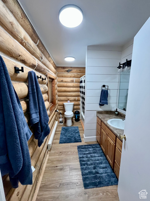 Bathroom with log walls, toilet, vanity, wood finished floors, and curtained shower