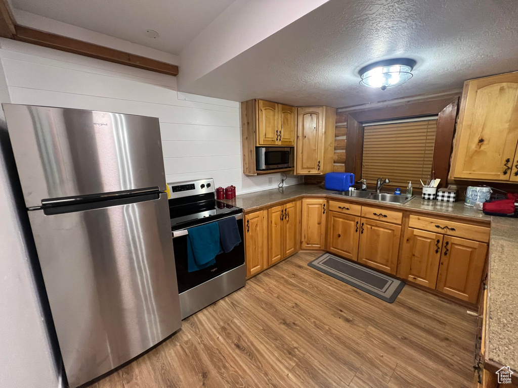 Kitchen with appliances with stainless steel finishes, a sink, light wood-style flooring, and a textured ceiling