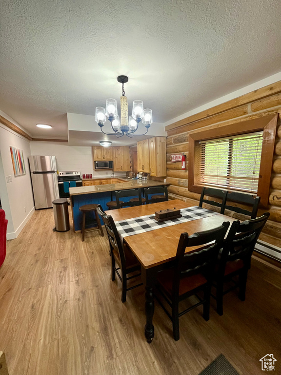 Dining space featuring log walls, light wood-type flooring, a textured ceiling, a chandelier, and baseboards
