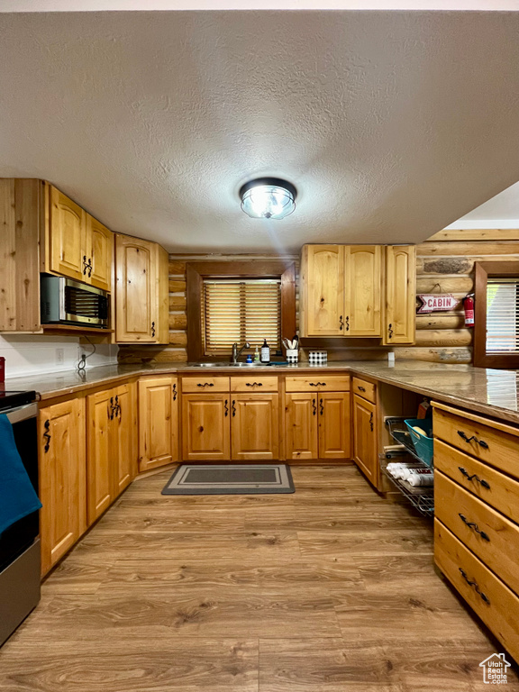 Kitchen with log walls, stainless steel microwave, light wood-type flooring, a sink, and a textured ceiling