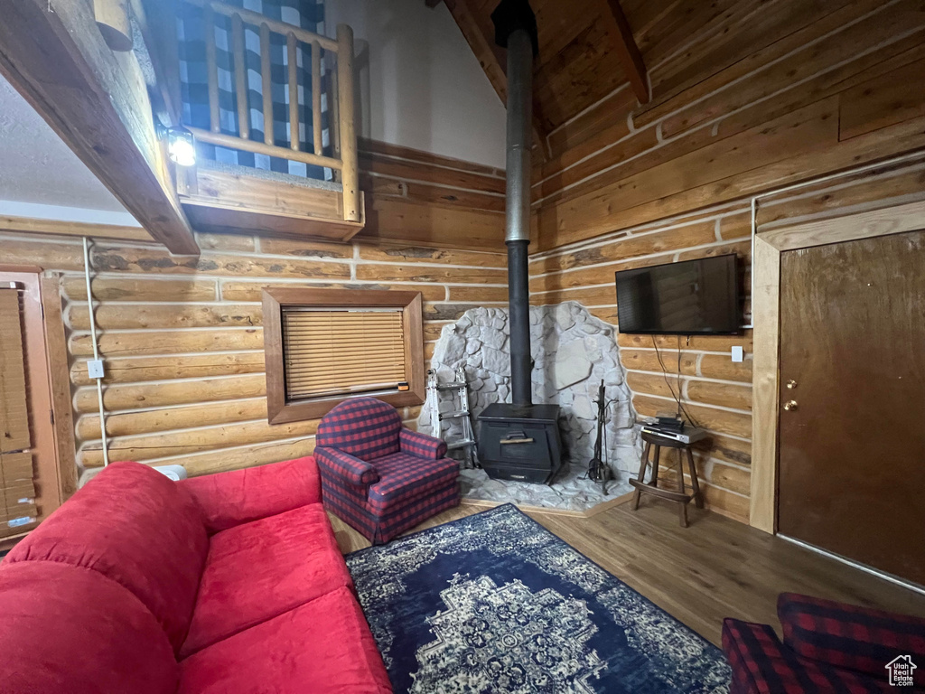 Living area with wood finished floors, a wood stove, beam ceiling, and rustic walls