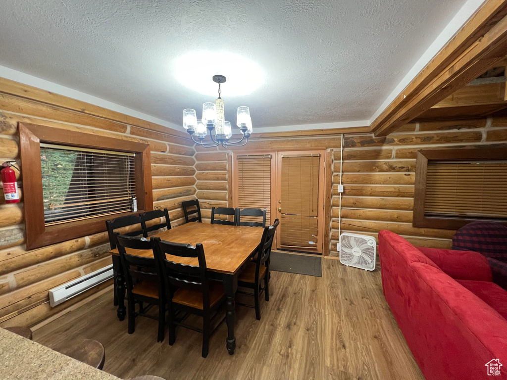 Dining space with rustic walls, a baseboard radiator, a chandelier, a textured ceiling, and wood finished floors