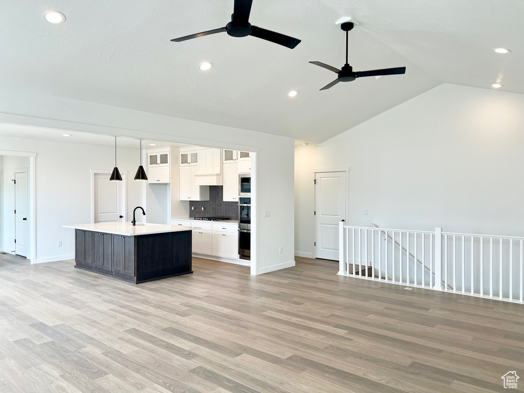 Kitchen featuring ceiling fan, a sink, white cabinetry, open floor plan, and high vaulted ceiling
