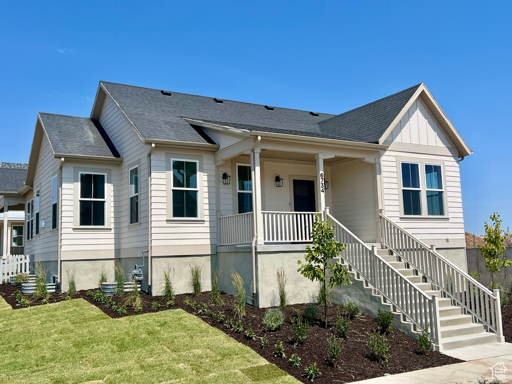 View of front of property with a porch, a front yard, stairway, and roof with shingles