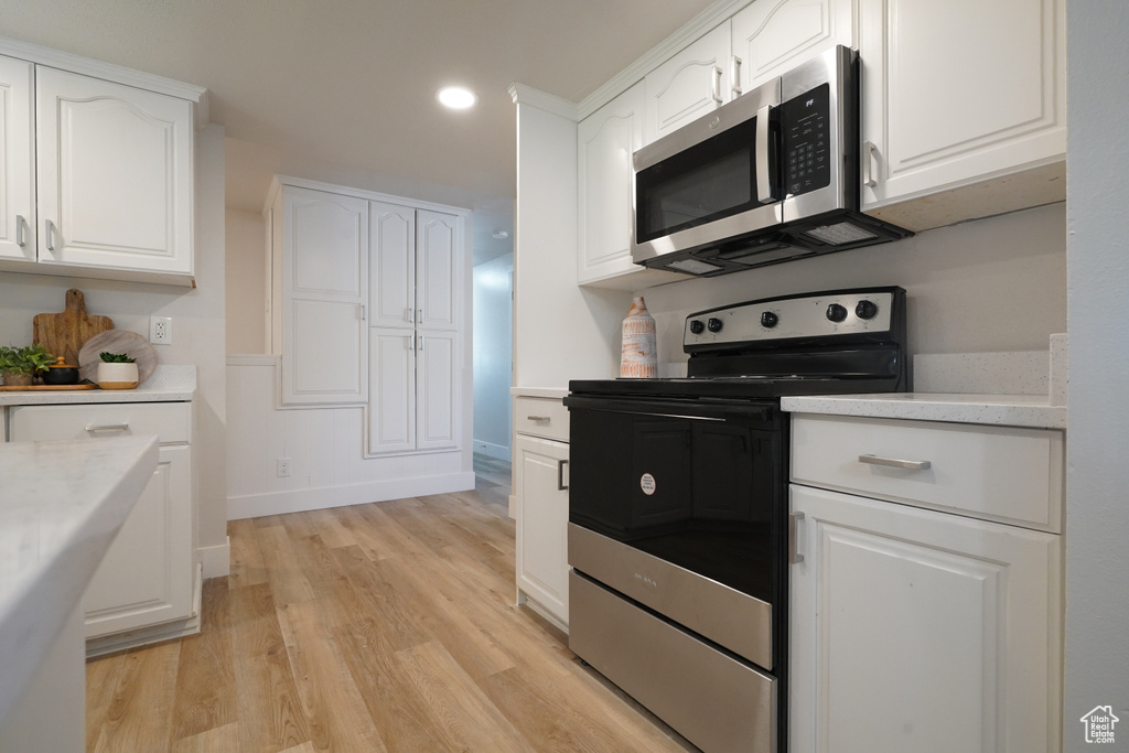 Kitchen with stainless steel appliances, white cabinetry, light wood-style flooring, light countertops, and recessed lighting