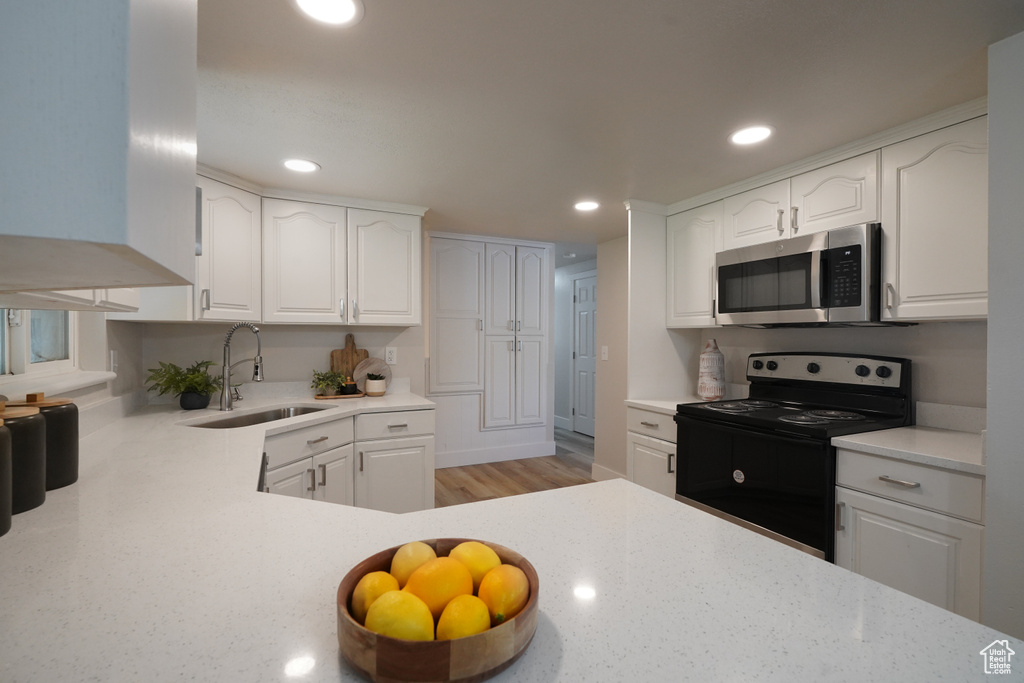Kitchen with stainless steel microwave, black electric range, a sink, white cabinetry, and recessed lighting