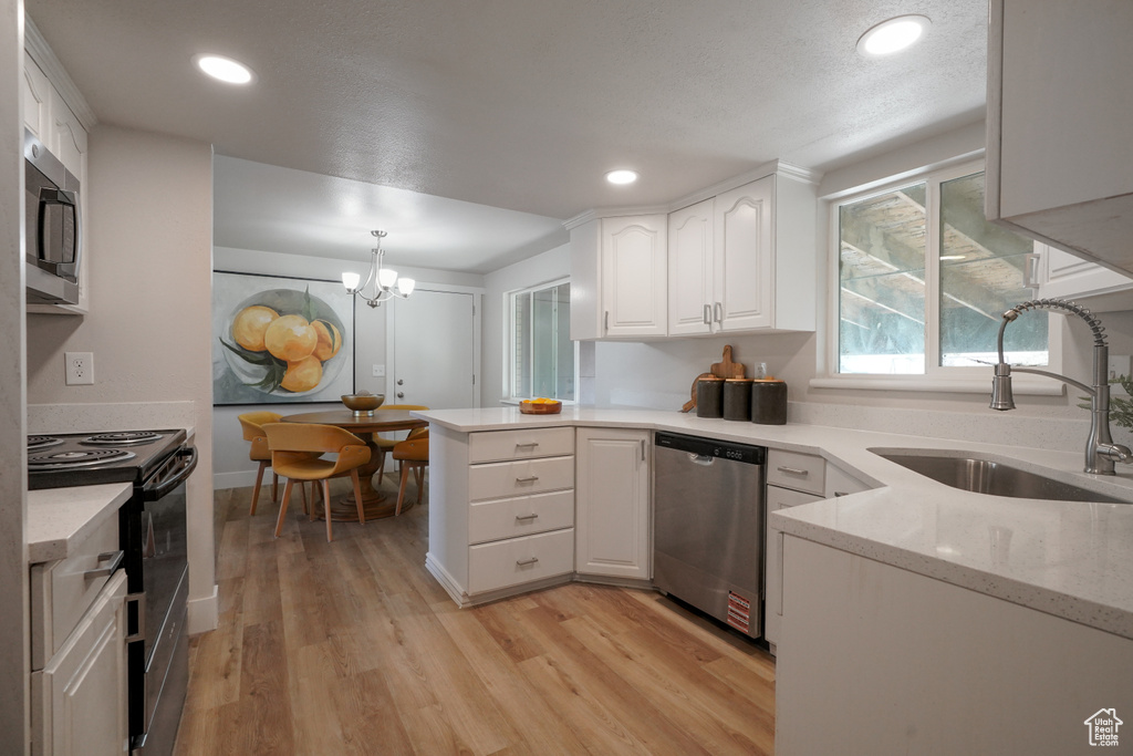 Kitchen with appliances with stainless steel finishes, a sink, white cabinets, light wood finished floors, and a peninsula