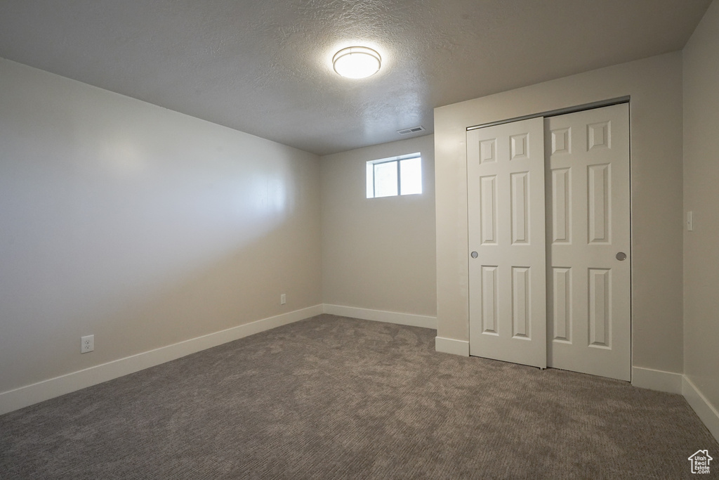 Unfurnished bedroom featuring baseboards, dark carpet, a textured ceiling, and a closet