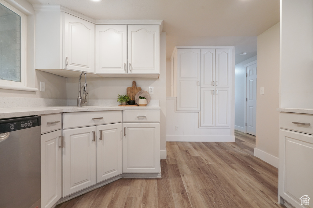 Kitchen featuring stainless steel dishwasher, light wood-style floors, white cabinets, baseboards, and light countertops