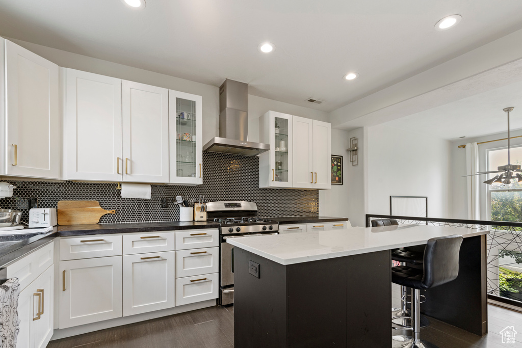 Kitchen featuring wall chimney exhaust hood, gas range, tasteful backsplash, a breakfast bar, and white cabinetry