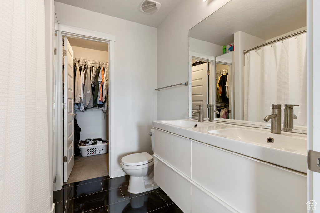 Full bath featuring toilet, tile patterned floors, double vanity, and a walk in closet