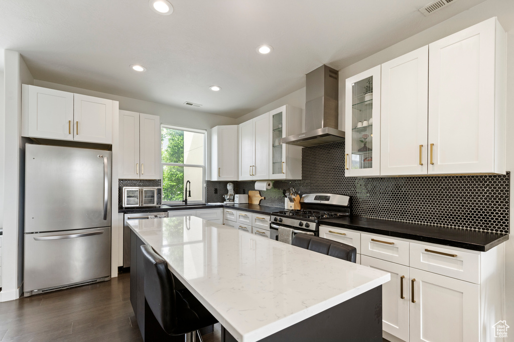Kitchen with appliances with stainless steel finishes, wall chimney exhaust hood, a sink, white cabinetry, and recessed lighting