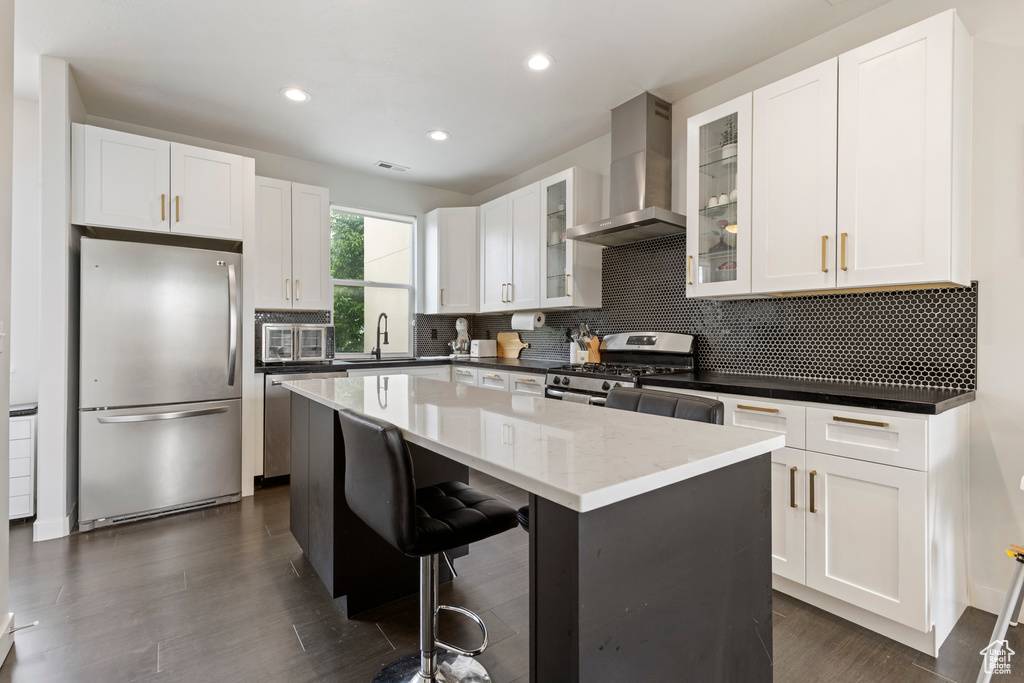 Kitchen with stainless steel appliances, wall chimney range hood, a center island, white cabinets, and decorative backsplash