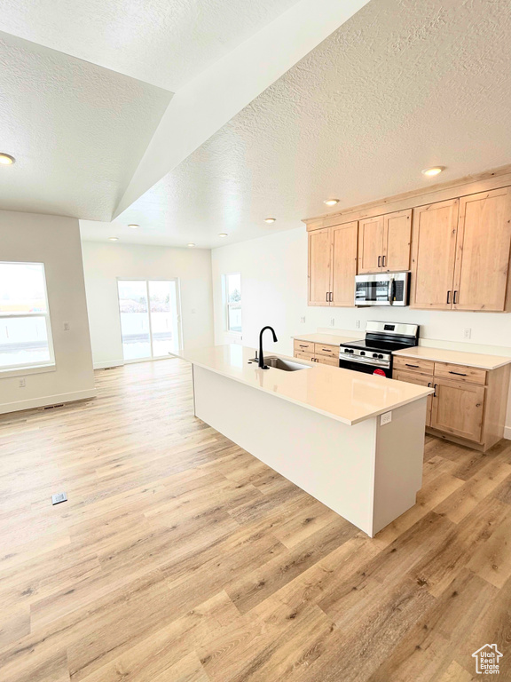 Kitchen with appliances with stainless steel finishes, a sink, light brown cabinets, light wood finished floors, and a textured ceiling