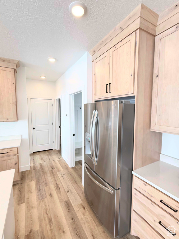 Kitchen with stainless steel refrigerator with ice dispenser, light brown cabinets, light wood-style flooring, a textured ceiling, and light countertops