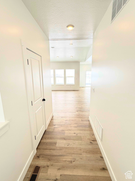 Corridor featuring light wood-type flooring, baseboards, and a textured ceiling