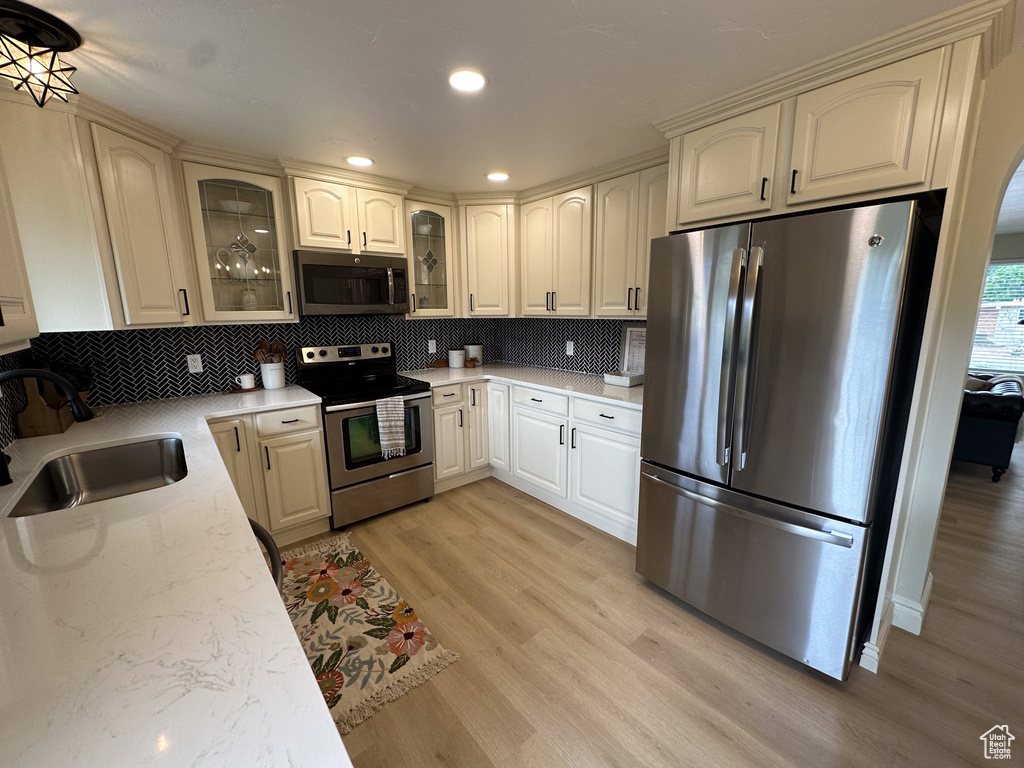 Kitchen featuring stainless steel appliances, a sink, light wood-style floors, decorative backsplash, and glass insert cabinets