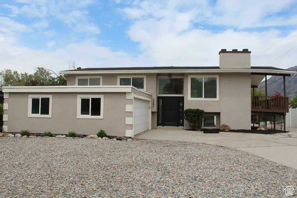 Bi-level home with driveway, a chimney, and stucco siding