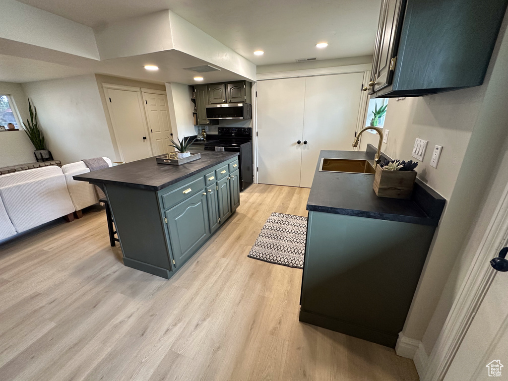 Kitchen featuring a sink, black electric range, stainless steel microwave, light wood-style flooring, and a breakfast bar area
