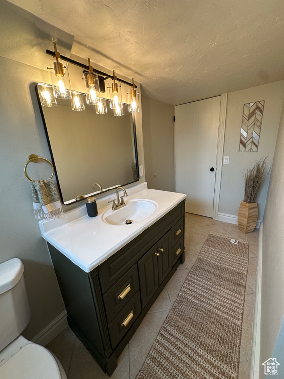 Bathroom with toilet, vanity, a textured ceiling, tile patterned flooring, and baseboards