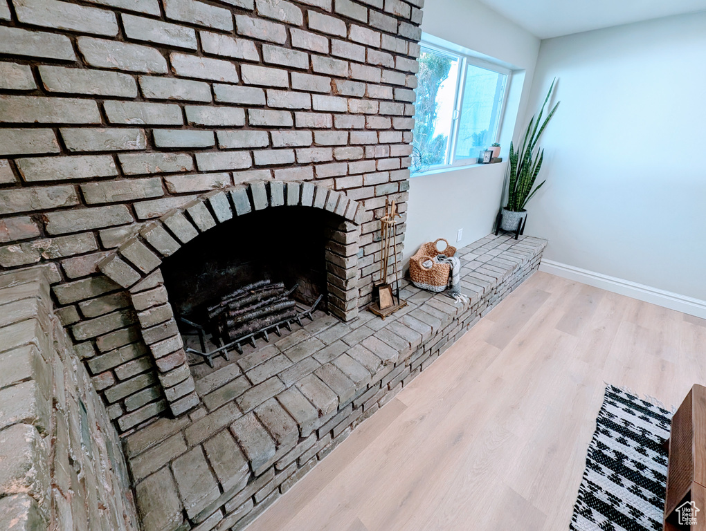 Detailed view of wood finished floors, a brick fireplace, and baseboards