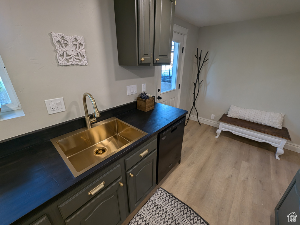Kitchen with black dishwasher, a sink, dark countertops, light wood finished floors, and baseboards