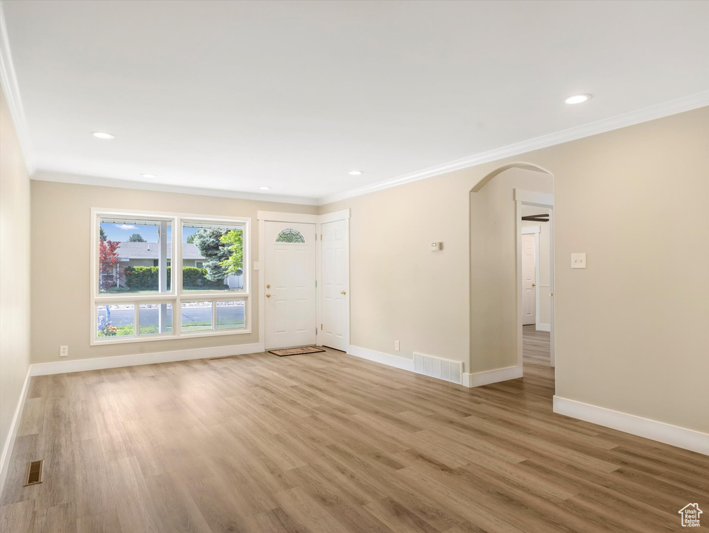 Unfurnished living room with arched walkways, crown molding, baseboards, light wood-type flooring, and recessed lighting