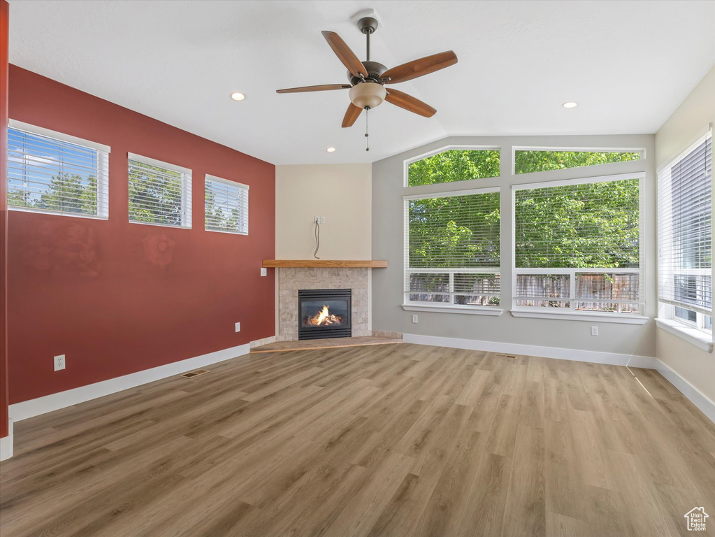 Unfurnished living room with a ceiling fan, wood finished floors, a tiled fireplace, vaulted ceiling, and baseboards